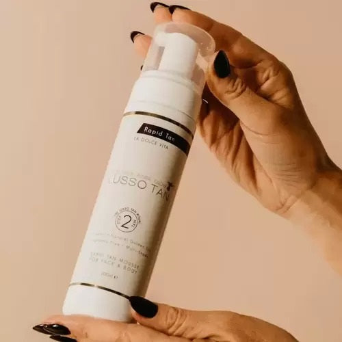 Hand holding a Lusso tan Rapid Express tanning product against a beige background