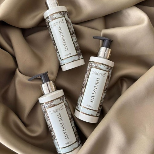 Three Lusso Tan bottles labeled 'The Instant' on a beige fabric background