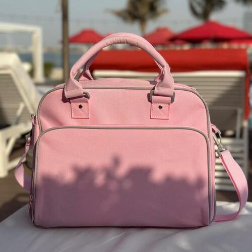 Pink baby bag on a table with beach chairs and umbrellas in the background