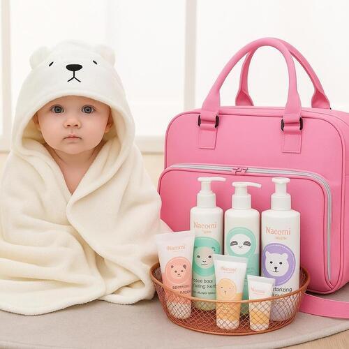 Baby in a white bear robe with a pink bag and nacomi baby care products on a light background
