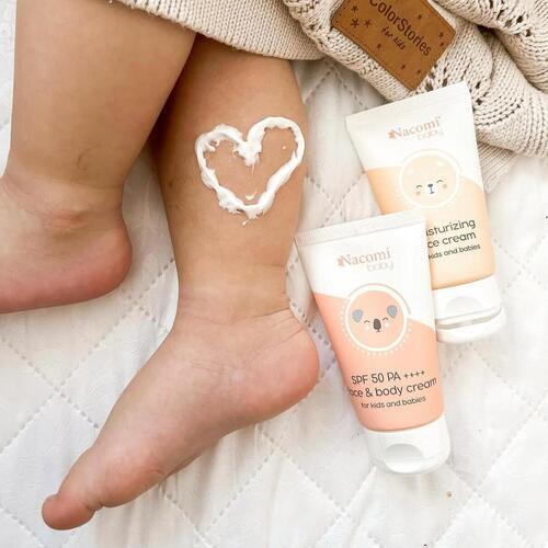 Baby legs with cream applied in a heart shape, next to Nacomi baby sunscreen bottles.
